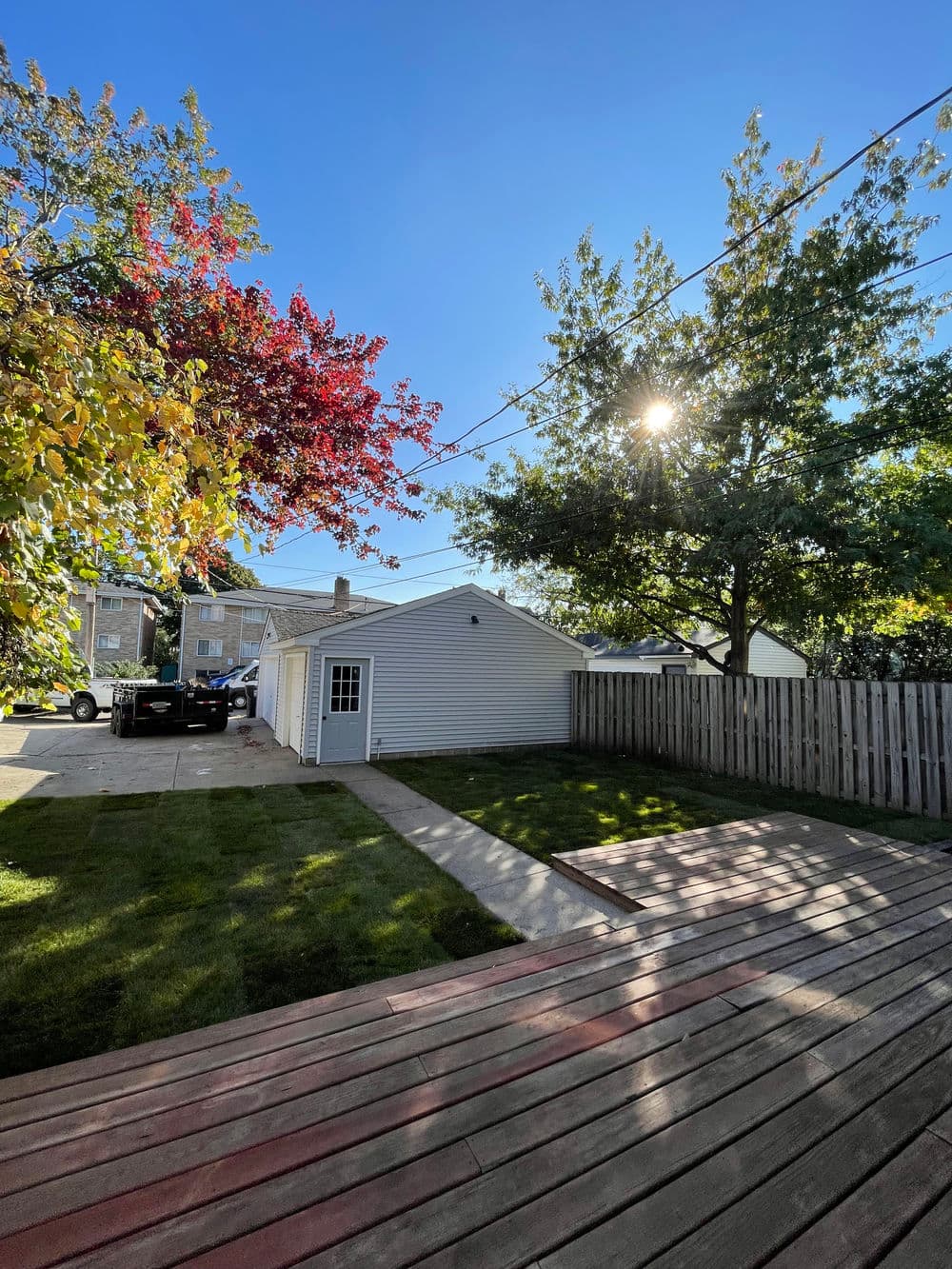 Bright backyard with trees, a garage, and a wooden deck under clear blue sky.